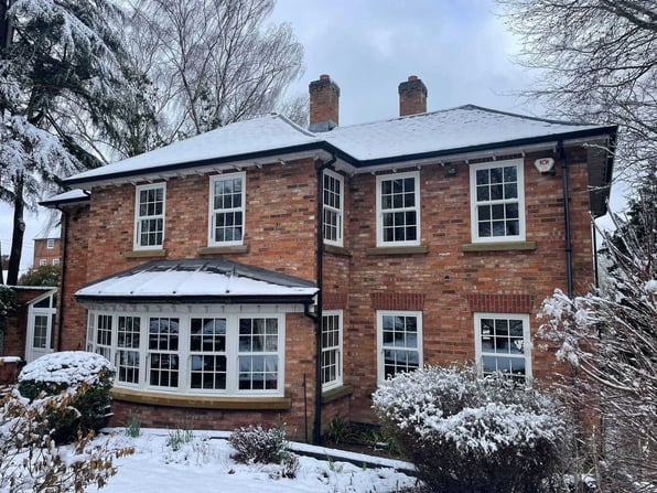 Snow-covered red-brick period home with white double-glazed sash windows and a ground-floor bay, showing energy-efficient glazing that suits a traditional property