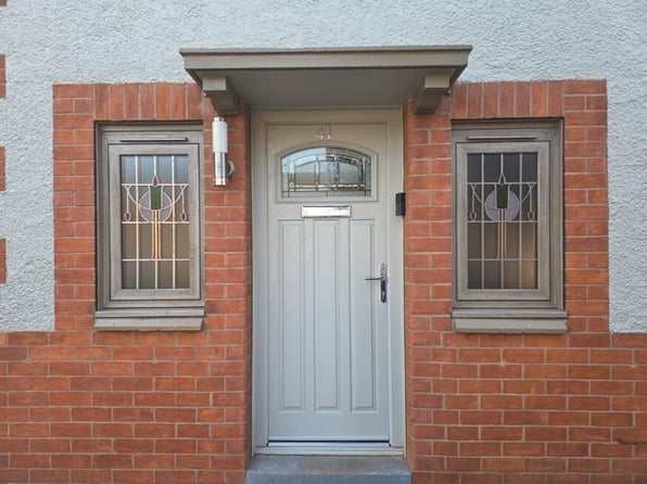 Grey composite front door installed on a brick home with decorative glazed side windows and a modern entrance design.