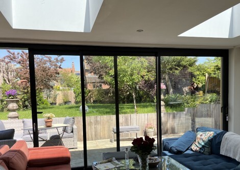 Modern living room with large aluminium doors and windows opening onto a landscaped garden. 