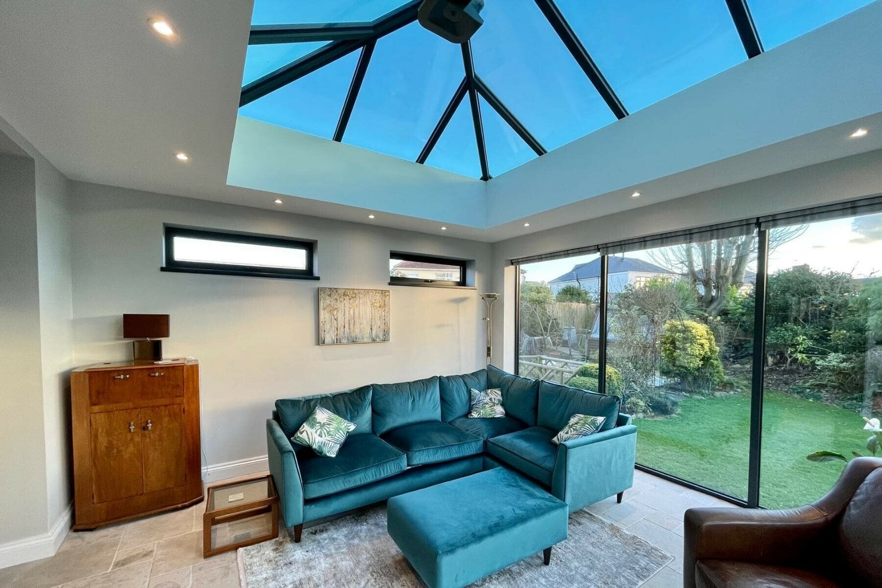 An ultraframe roof extension being used as a living room with views onto the garden with someone trying to decide which ultra room extension to install 